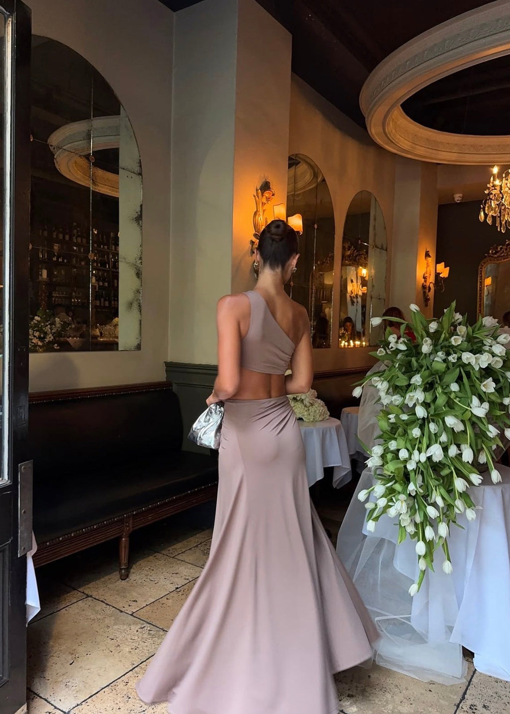 Model wearing the Ance Gria Serena Maxi Dress in Taupe, designed with a one-shoulder bodice, soft draping, gathered waist with a statement ring detail, side cut-out and an elegant floor-length skirt with an asymmetrical hem.