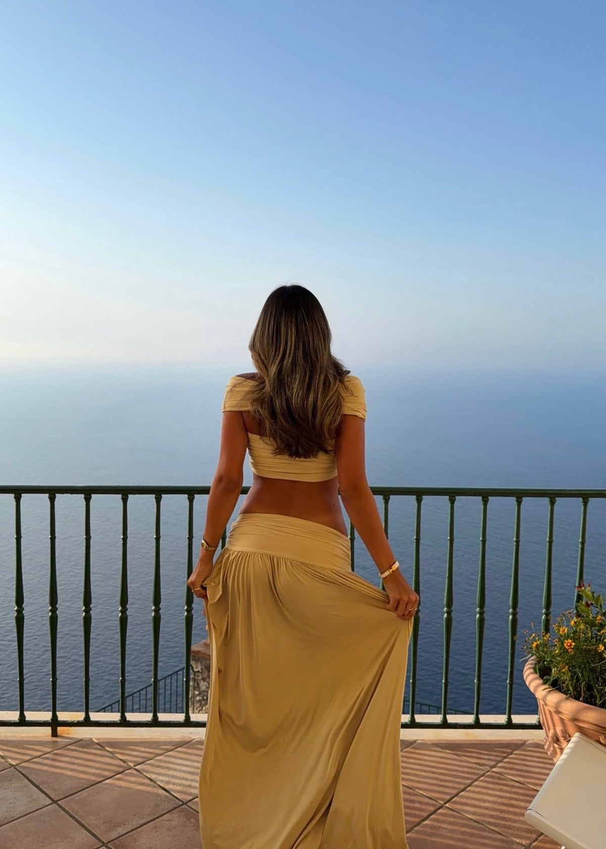 Model wearing the Arcina Ori Alessia Set in Sand, featuring an off-the-shoulder twist-front crop top with draped short sleeves and gathered bust detailing, paired with a low-rise maxi skirt with a gathered waistband, soft draping and a floor-length flowing silhouette.
