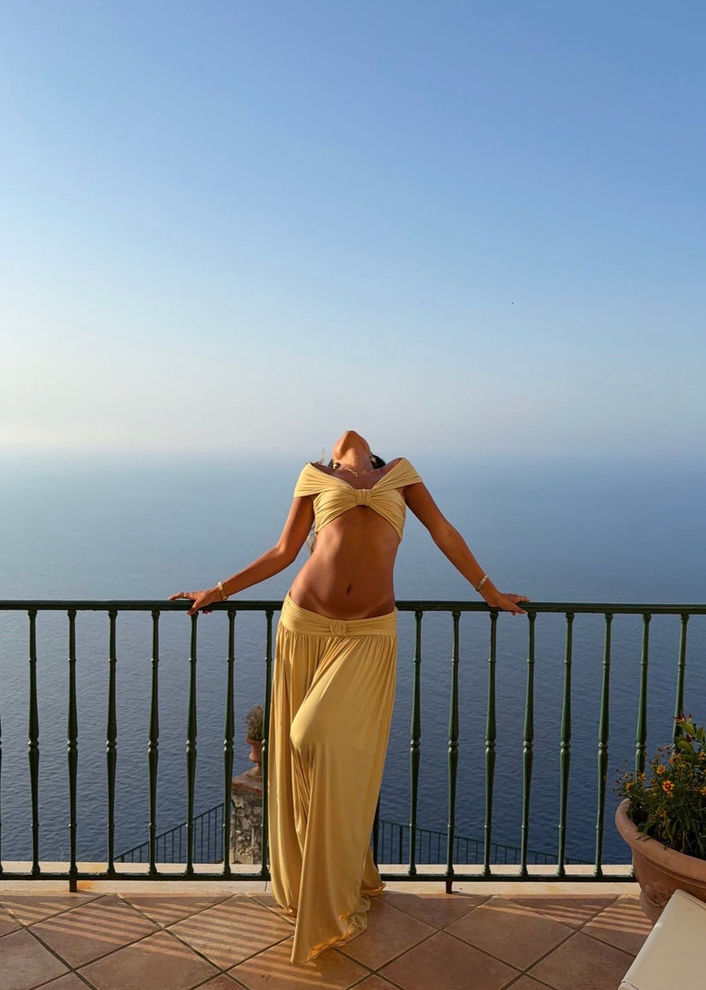 Model wearing the Arcina Ori Alessia Set in Sand, featuring an off-the-shoulder twist-front crop top with draped short sleeves and gathered bust detailing, paired with a low-rise maxi skirt with a gathered waistband, soft draping and a floor-length flowing silhouette.