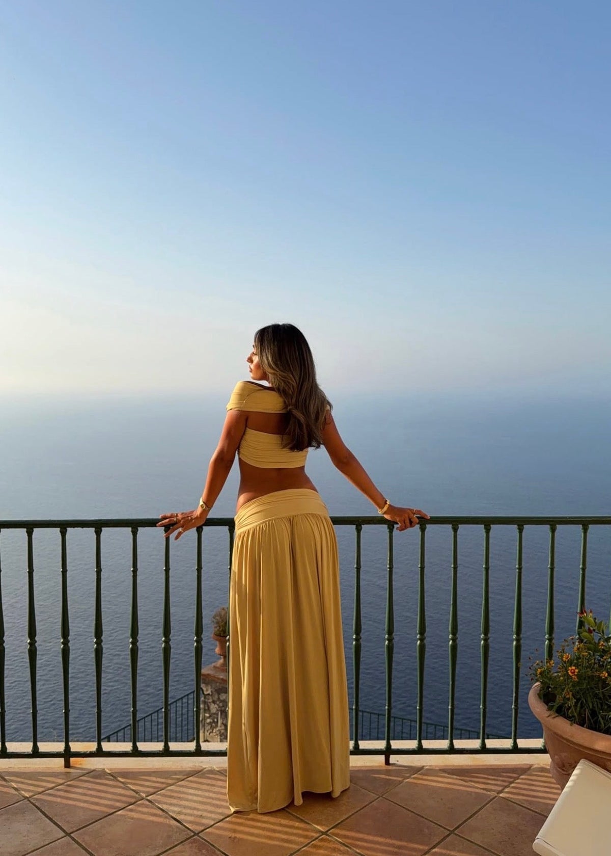 Model wearing the Arcina Ori Alessia Set in Sand, featuring an off-the-shoulder twist-front crop top with draped short sleeves and gathered bust detailing, paired with a low-rise maxi skirt with a gathered waistband, soft draping and a floor-length flowing silhouette.