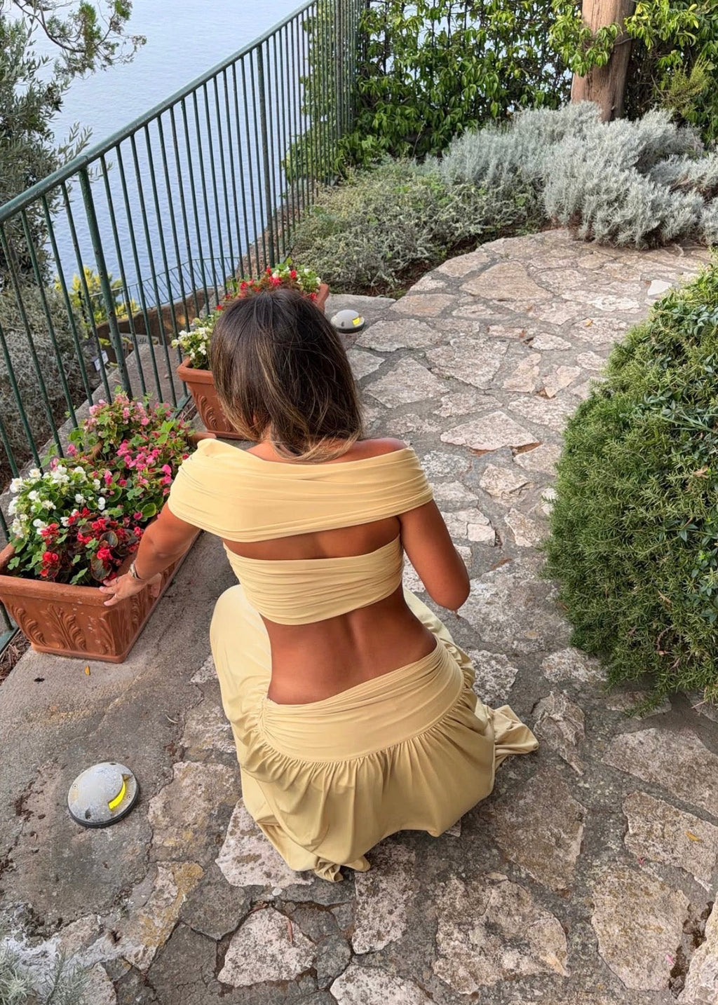 Model wearing the Arcina Ori Alessia Set in Sand, featuring an off-the-shoulder twist-front crop top with draped short sleeves and gathered bust detailing, paired with a low-rise maxi skirt with a gathered waistband, soft draping and a floor-length flowing silhouette.