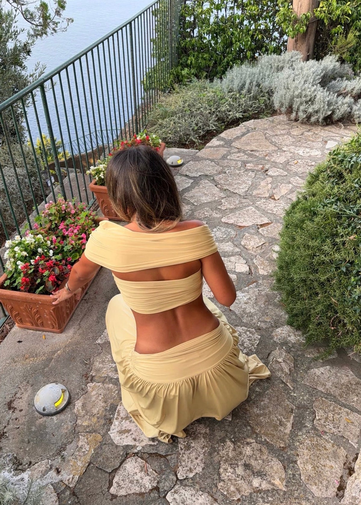 Model wearing the Arcina Ori Alessia Set in Sand, featuring an off-the-shoulder twist-front crop top with draped short sleeves and gathered bust detailing, paired with a low-rise maxi skirt with a gathered waistband, soft draping and a floor-length flowing silhouette.